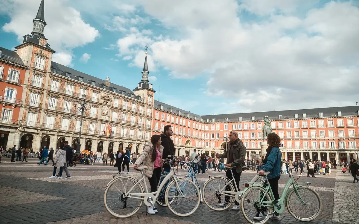 Two riders crossing the arcaded Plaza Mayor in Madrid with their bikes