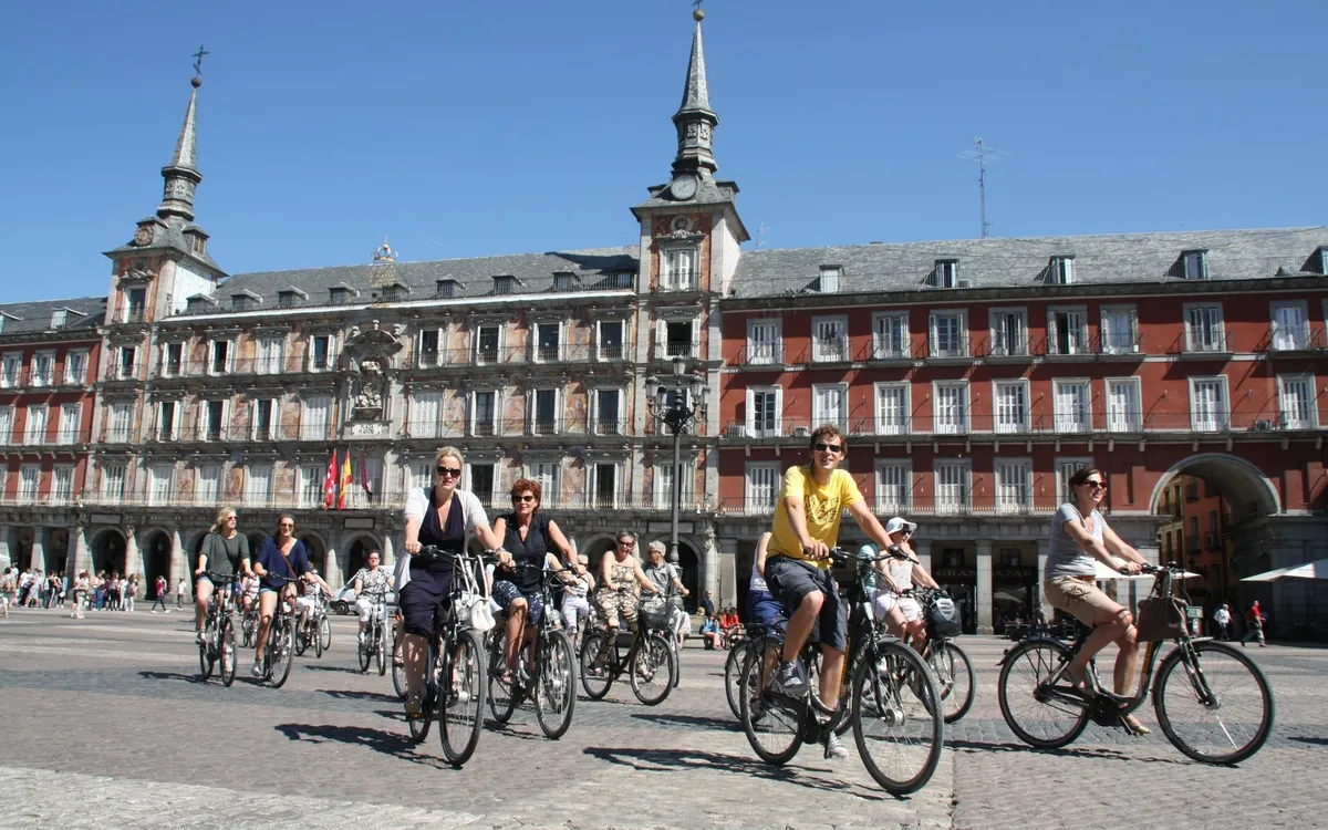 Riders crossing the Plaza Mayor on city bikes, the red-brick arcades of the square behind them