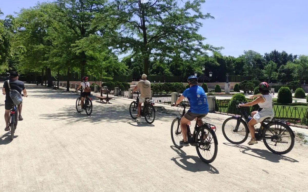 Cyclists on a wide tree-lined path through Retiro Park on a sunny afternoon