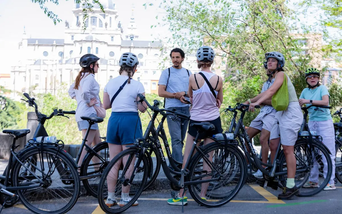 A group in helmets with their bikes on the forecourt below the domes of the Almudena Cathedral and the Royal Palace