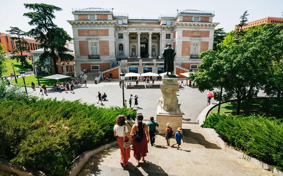 The long facade of the Prado Museum seen across its gardens, with visitors on the path in front