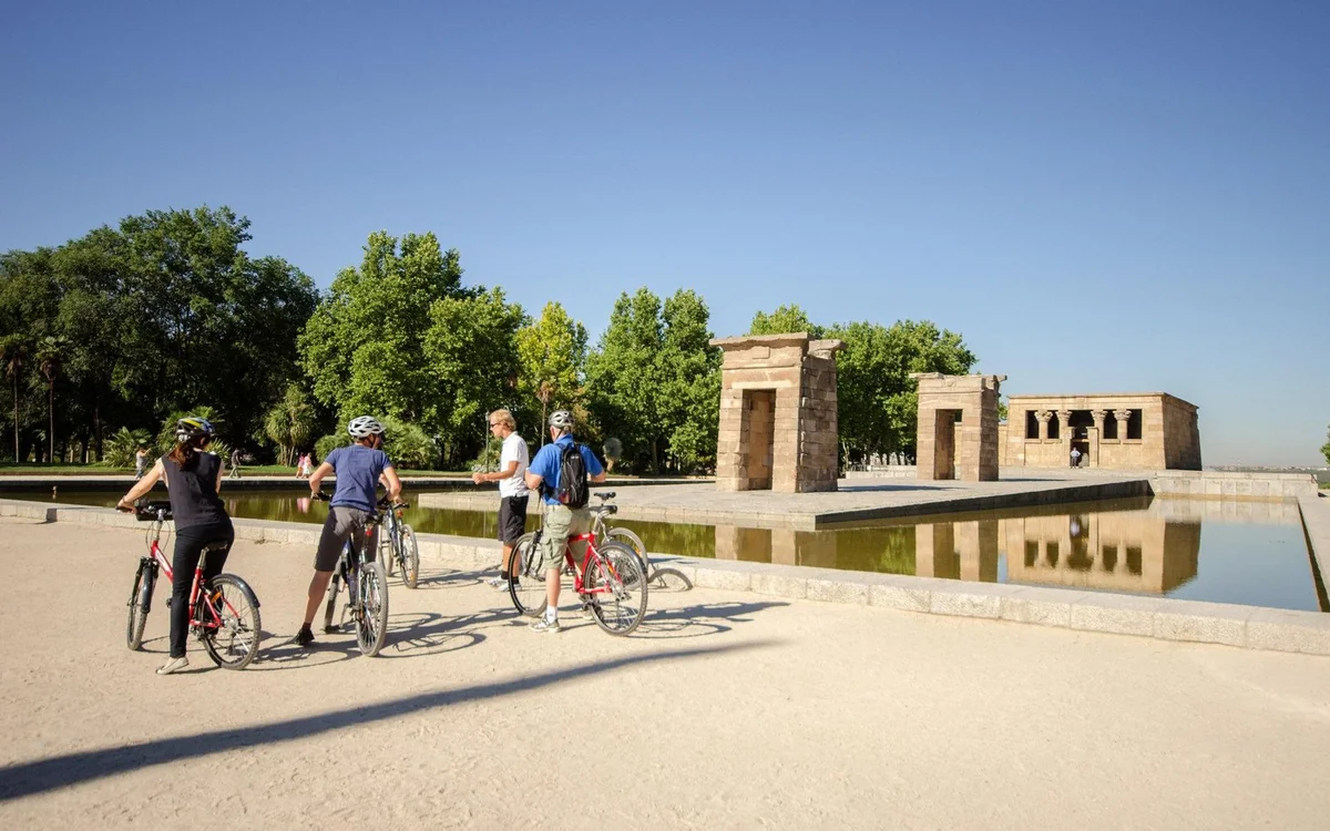 Riders standing with their bikes beside the still pool in front of the stone gateways of the Temple of Debod